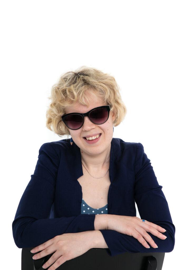 Anna is wearing sunglasses and a suit jacket, looking at the camera