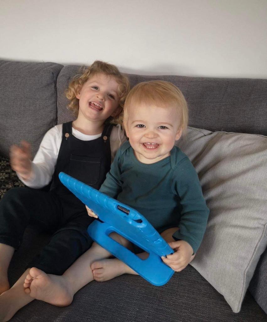Cian sat with his sister on a sofa smiling. He is holding an ipad
