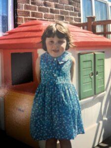Natalie as a child in front of a playhouse
