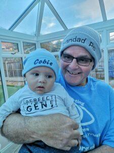 Smiling with his baby grandon, wearing hats with their names on