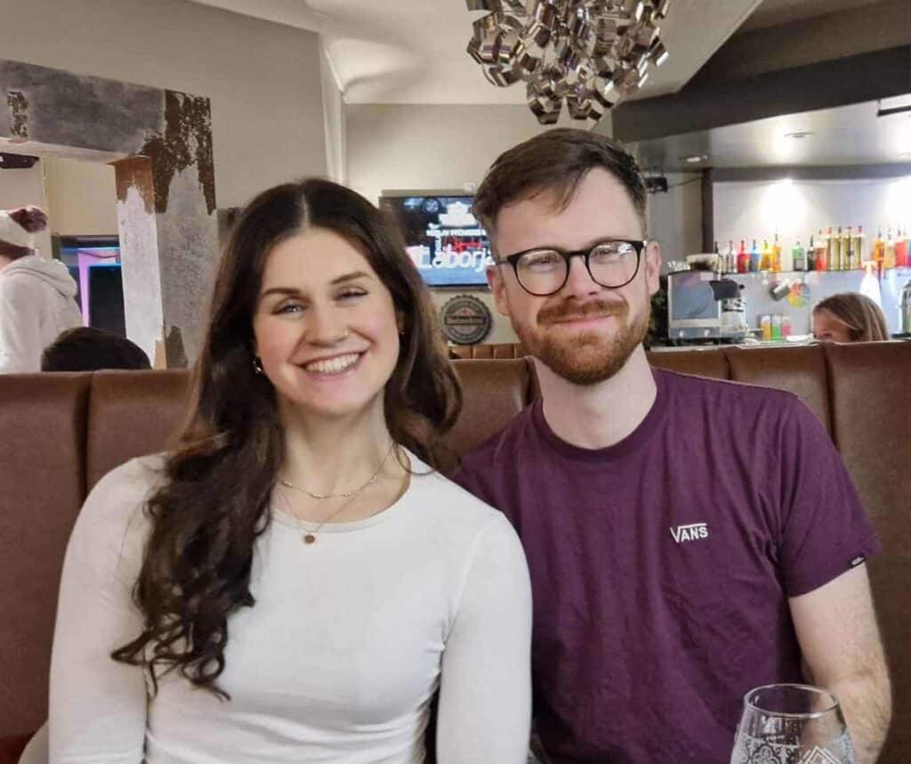 Beth and Ross are sat together smiling