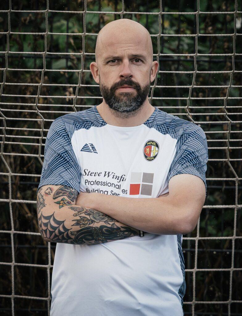 Rich has his arms crossed for his footbalk headshot. He is wearing the kit